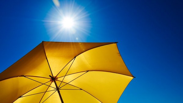 Sonnenschirm Hitze UV-Schutz Ein gelber Sonnenschirm vor einem strahlend blauen Himmel mit Sonne.