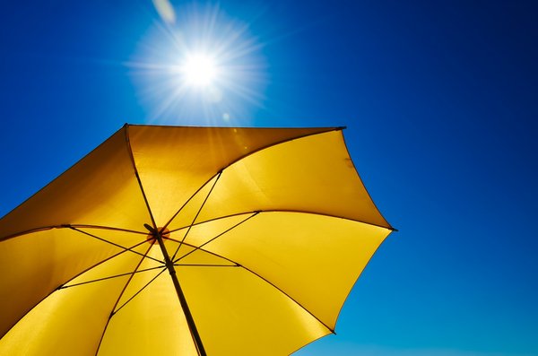 Sonnenschirm Hitze UV-Schutz Ein gelber Sonnenschirm vor einem strahlend blauen Himmel mit Sonne.